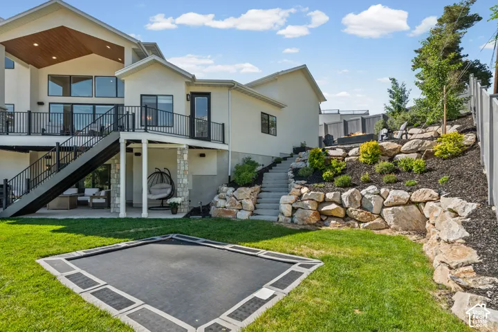 Multi-level backyard featuring a manicured lawn, built-in trampoline, and extensive rock landscaping with planted beds