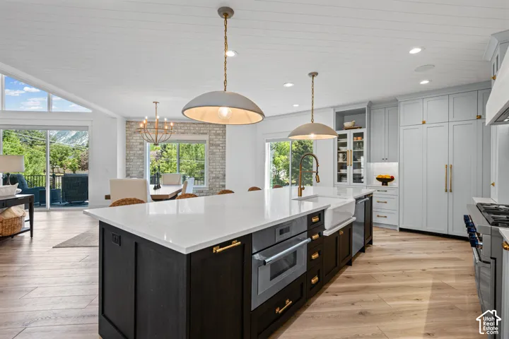 Spacious kitchen featuring a large central island with white countertop, integrated microwave, farmhouse-style sink, and gold-tone hardware