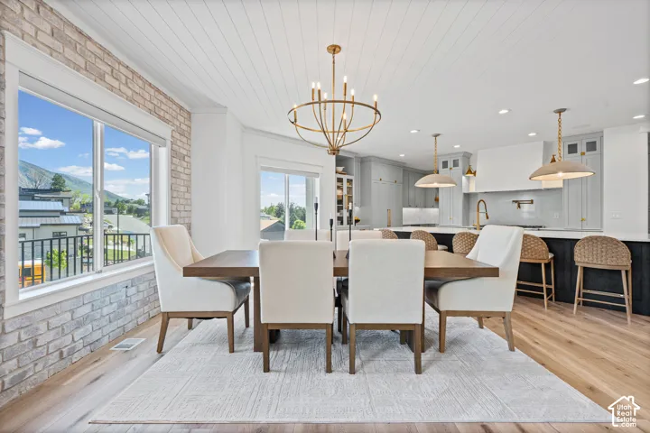 Open-concept dining and kitchen space featuring a large window, wood-finish flooring, a white shiplap ceiling, a contemporary brass chandelier, and a kitchen island with pendant lighting