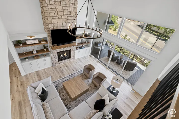 Two-story living room featuring a stone fireplace with a wood-mantle, built-in cabinetry, and wood-finish flooring