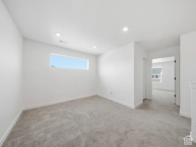 Spacious room featuring a horizontal window, recessed lighting, neutral carpeting, white baseboards, and a doorway to an additional room