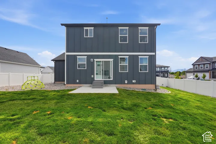 Spacious backyard featuring a concrete patio, sliding glass door access, white vinyl fencing, and a gravel perimeter