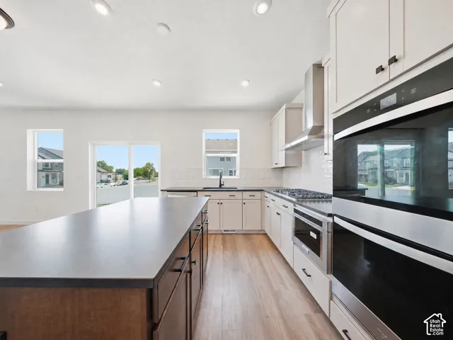 Kitchen featuring a large island with a dark countertop, light wood-finish flooring, white cabinetry, integrated stainless steel appliances, and a subway tile backsplash