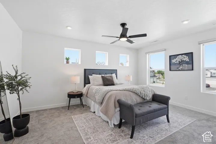 Spacious room featuring light gray carpet, white walls, multiple windows, a ceiling fan with light, and recessed lighting