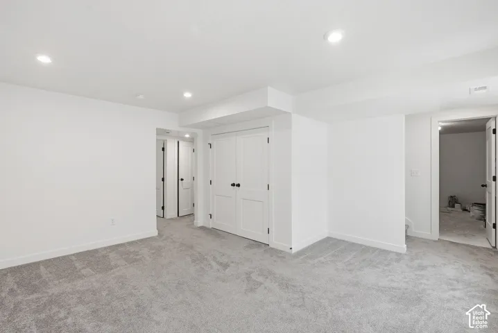 Spacious room featuring light gray carpet flooring, recessed lighting, white walls, and multiple paneled doors with black hardware