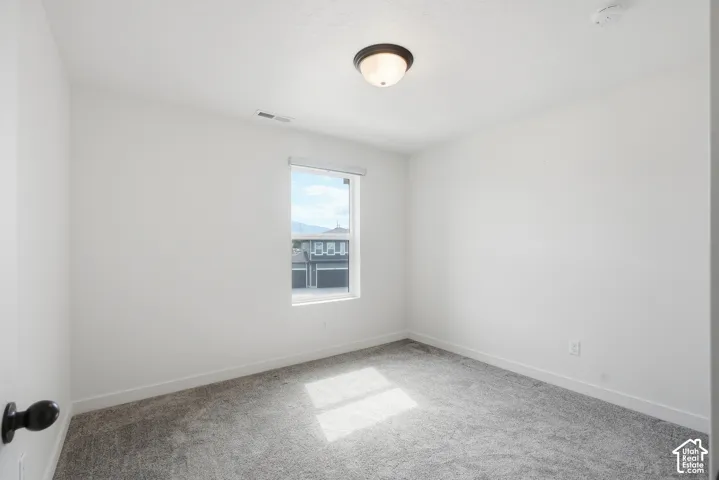Bright interior space featuring a single window, overhead flush mount lighting, light gray carpeting, crisp white walls, and a visible electrical outlet