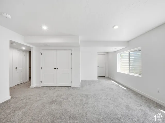 Spacious room featuring light gray carpeting, recessed ceiling lighting, a window with horizontal blinds, and white paneled doors with matte black hardware