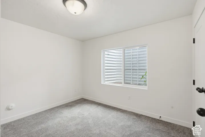 Carpeted room with a white door featuring matte black hardware, a window with a window well, and a flush mount ceiling light