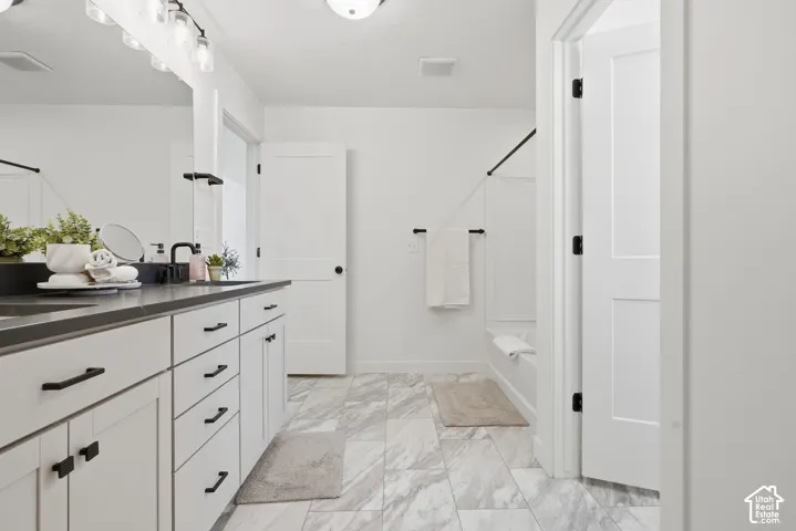 Bathroom featuring a dual vanity with a dark countertop and white cabinetry, marble-look floor tiling, a built-in bathtub with subway tile surround, and matte black fixtures