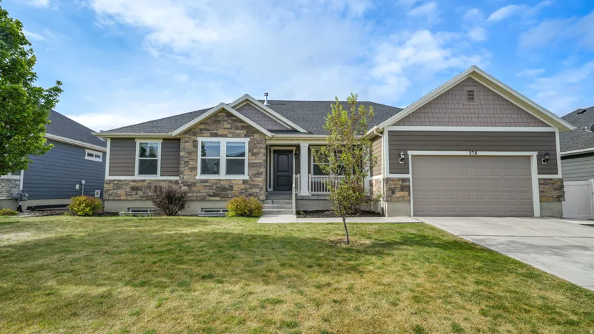 Ranch-style exterior featuring stone and siding finishes, an attached two-car garage, covered front porch, and mature landscaping