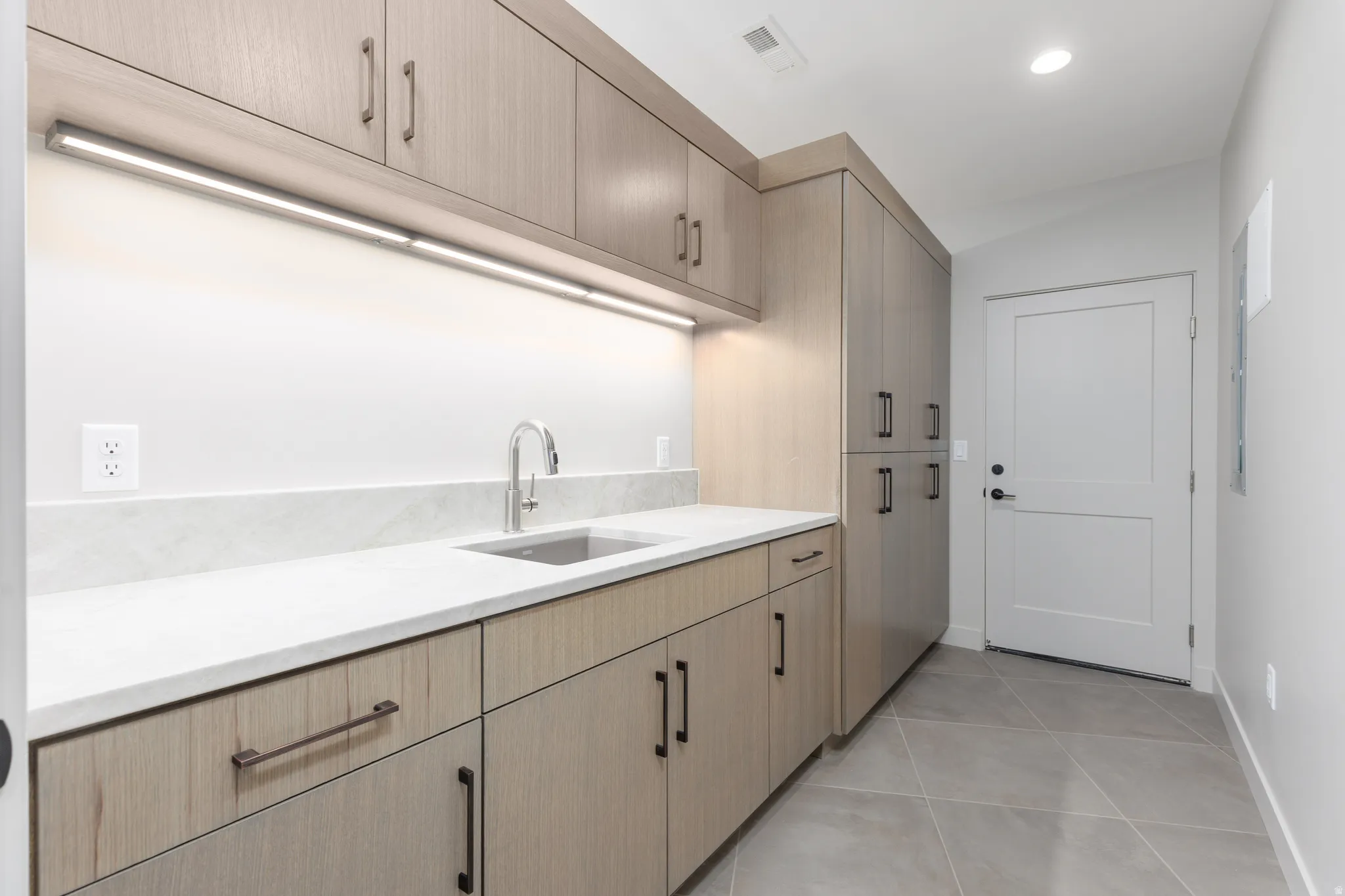 Large laundry room featuring custom cabinets and a sink which leads from the garage to a custom locker area. Perfect for keeping shoes and coats organized.