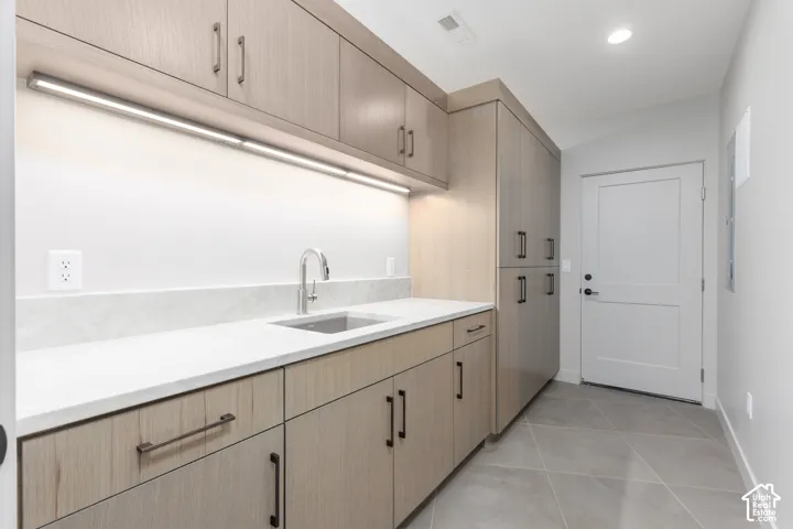 Large laundry room featuring custom cabinets and a sink which leads from the garage to a custom locker area. Perfect for keeping shoes and coats organized.
