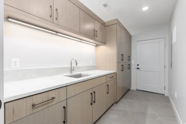 Large laundry room featuring custom cabinets and a sink which leads from the garage to a custom locker area. Perfect for keeping shoes and coats organized.