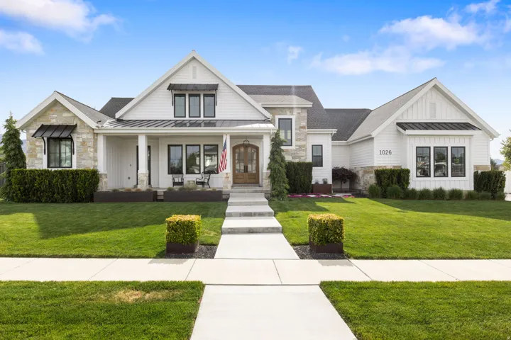 Modern farmhouse exterior featuring white siding, stone accents, black-framed windows, a covered front porch, and a concrete pathway leading to the entry