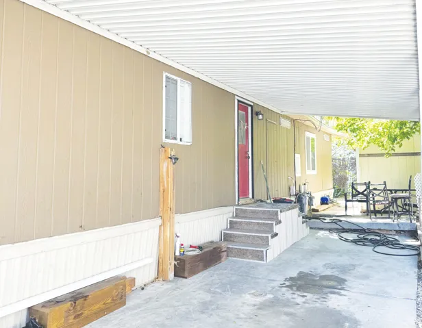 Covered outdoor area featuring a concrete pad, a white corrugated metal awning, and exterior steps leading to a red entry door