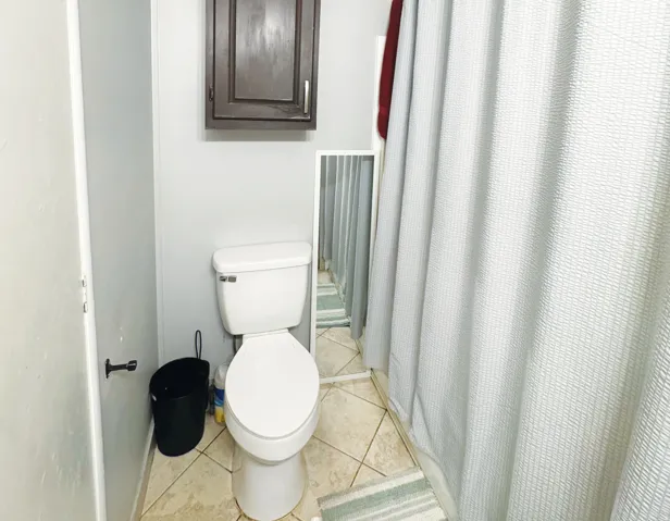 Bathroom with ceramic tile flooring, a white toilet, and a dark wood-finish wall-mounted cabinet