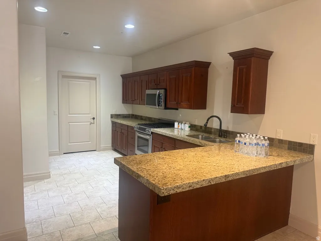 Kitchenette featuring granite countertops, wood cabinetry, stainless steel appliances, and tile flooring
