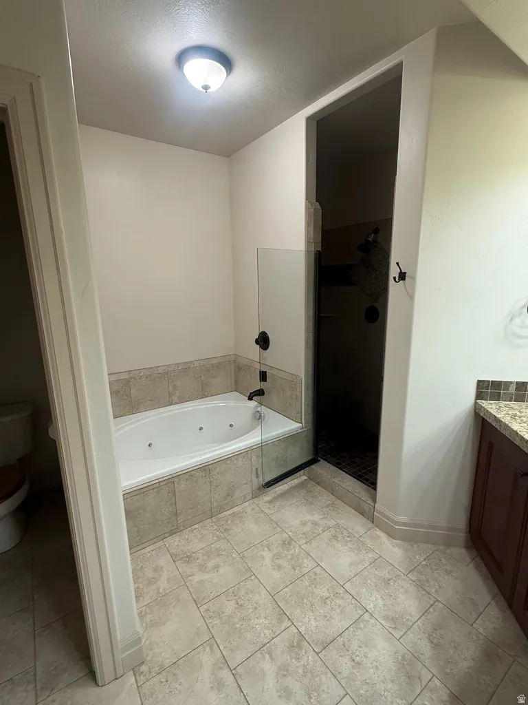 Tiled bathroom featuring a jetted soaking tub with a tiled surround, a separate shower with a glass enclosure, and stone-look floor tiles
