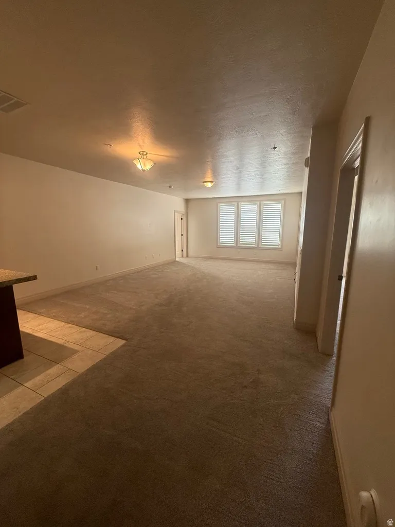 Spacious interior room featuring light beige walls and a combination of carpet and tile flooring