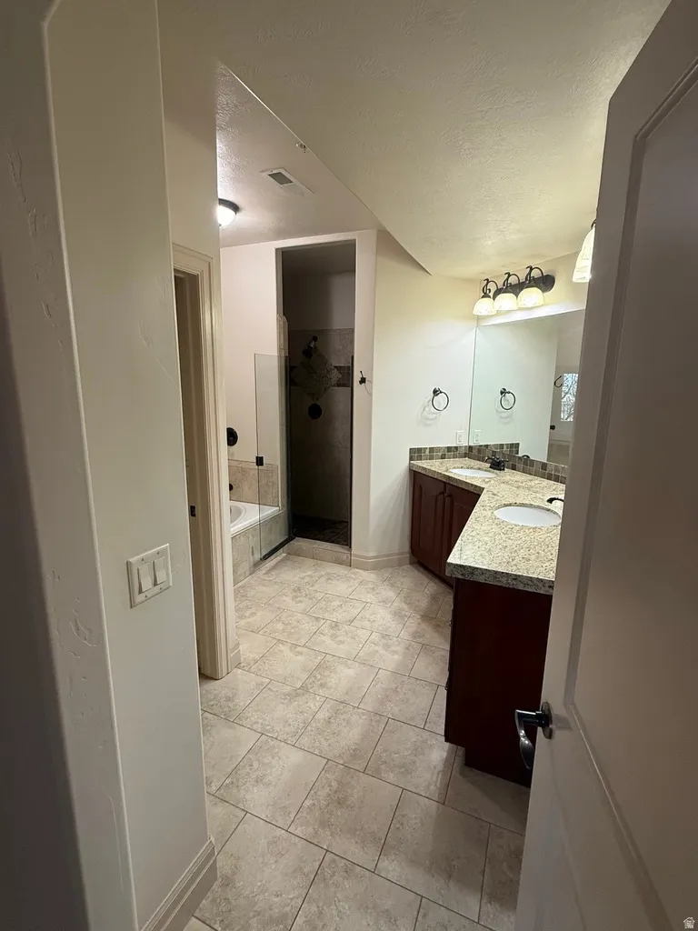 Bathroom featuring dual vanities with granite countertops, tile flooring, a glass-enclosed shower, and a built-in bathtub
