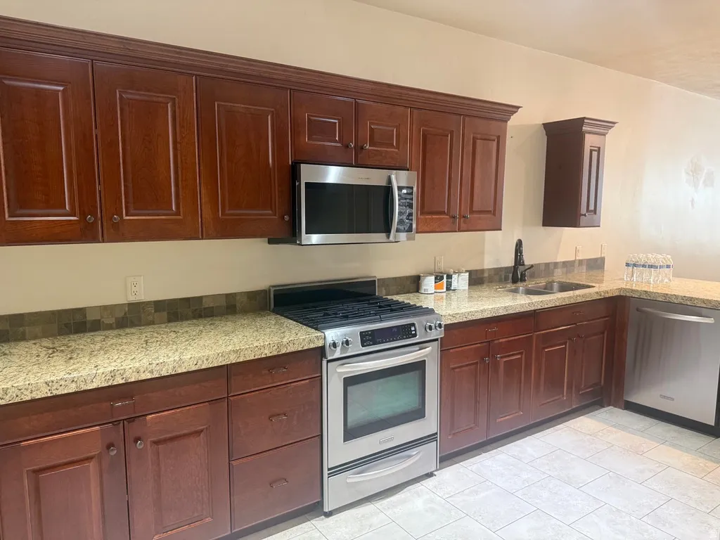Kitchen featuring dark wood cabinetry, light granite-finish countertops, and a mosaic tile backsplash