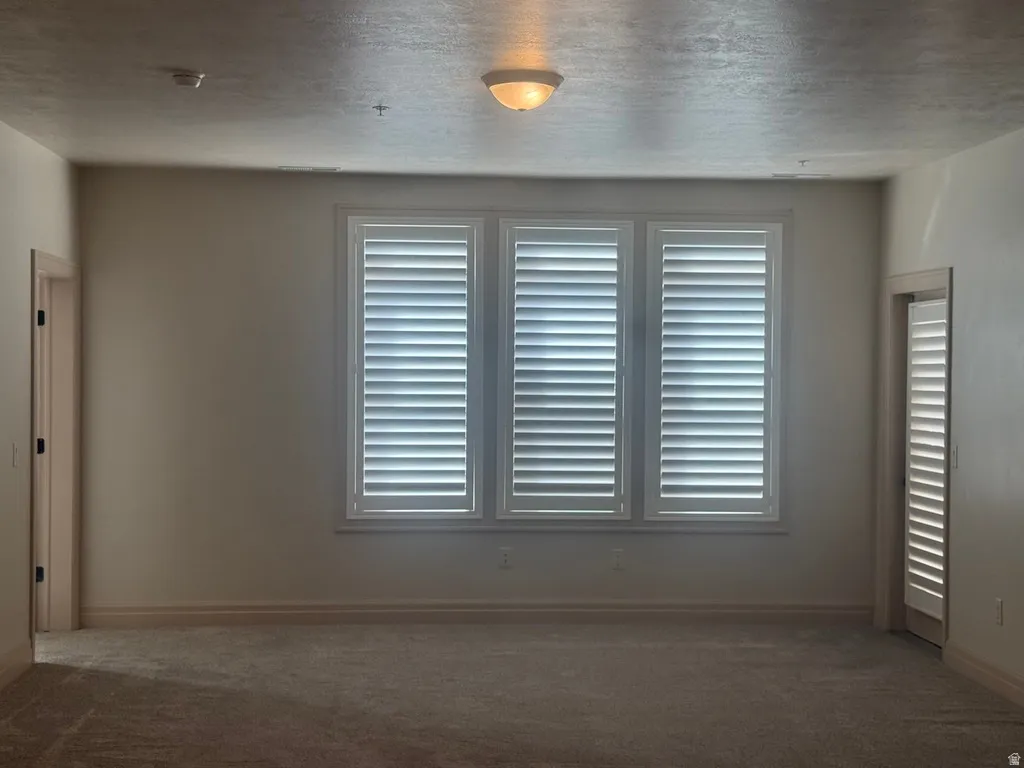 Triple window with plantation shutters, neutral tone walls, recessed lighting, and carpet flooring