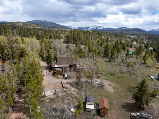 Mountain property surrounded by mature trees, featuring a multi-story residence with a brown roof and a detached shed