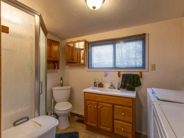 Bathroom featuring a glass-enclosed shower, a vanity with wood-finish cabinetry, a window with blinds, and tile flooring