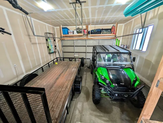 Spacious garage featuring high ceilings, fluorescent lighting, a roll-up garage door, overhead storage shelving, and a side window