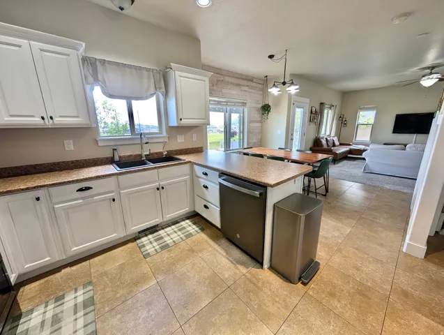 Open-concept kitchen featuring an integrated dishwasher, white cabinetry, dark countertop, and tile flooring