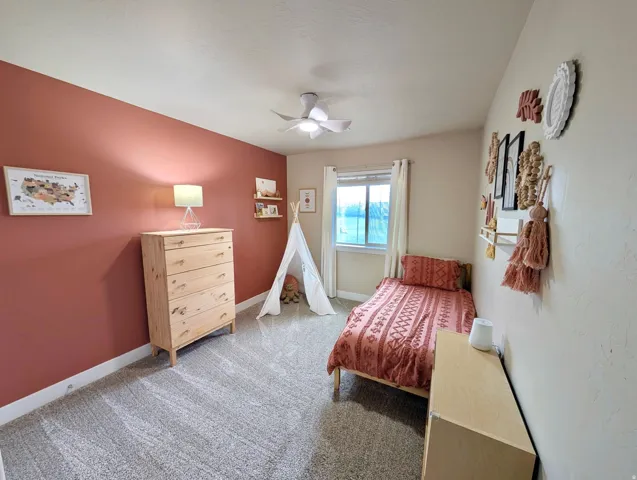 Carpeted room featuring a single window with white trim, a ceiling fan, and a painted accent wall