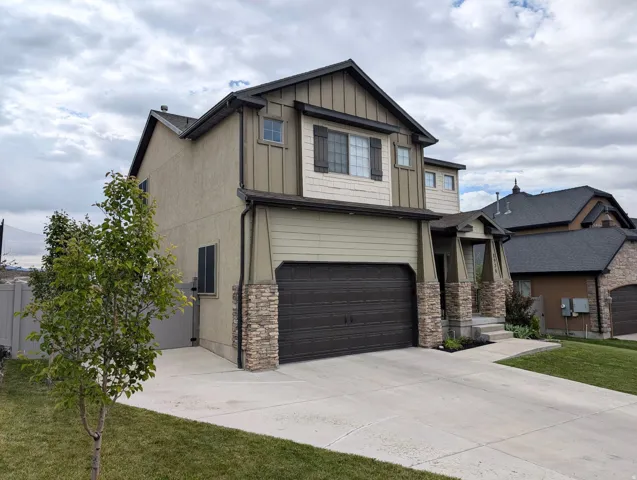 Contemporary stucco and siding exterior featuring stone veneer accents, a dark-paneled garage door, a prominent front entry with stone-clad columns, a concrete driveway, and established front landscaping