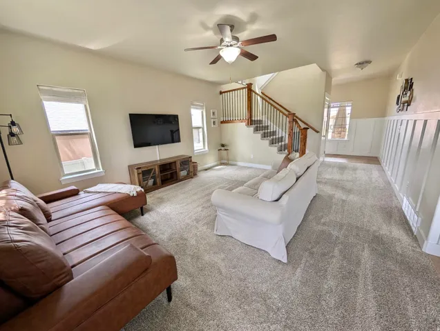 Spacious living area featuring neutral carpeting, a staircase with wood newel posts and metal balusters, and a ceiling fan