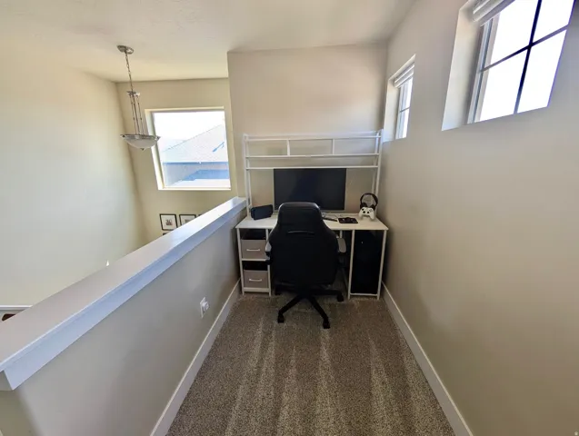 Carpeted loft area featuring a low wall, multiple windows for natural light, and a built-in light fixture