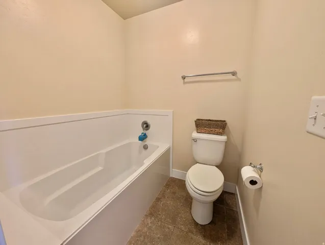 Bathroom featuring a white bathtub with a chrome faucet, a white toilet, neutral wall paint, and tiled flooring