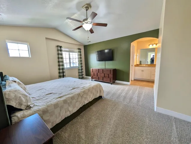 Spacious room featuring vaulted ceilings, plush carpet flooring, and an arched doorway leading to a vanity area