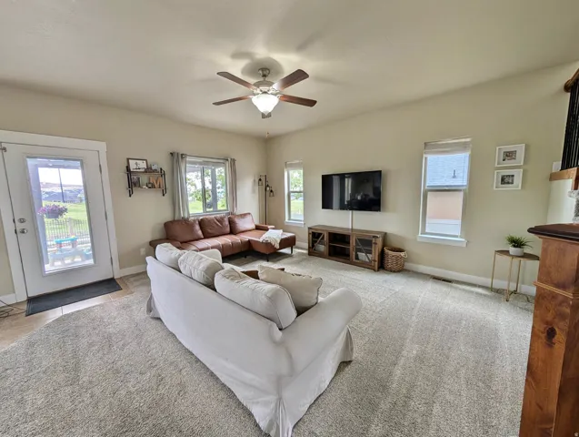 Spacious living area featuring neutral carpeting, a ceiling fan with integrated lighting, and multiple windows for abundant natural light
