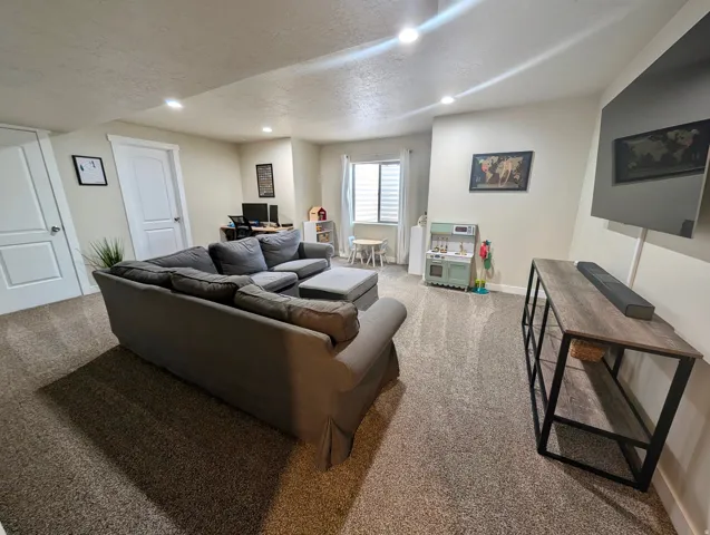 Spacious room featuring neutral carpeting, recessed lighting, a window with blinds, and white interior doors