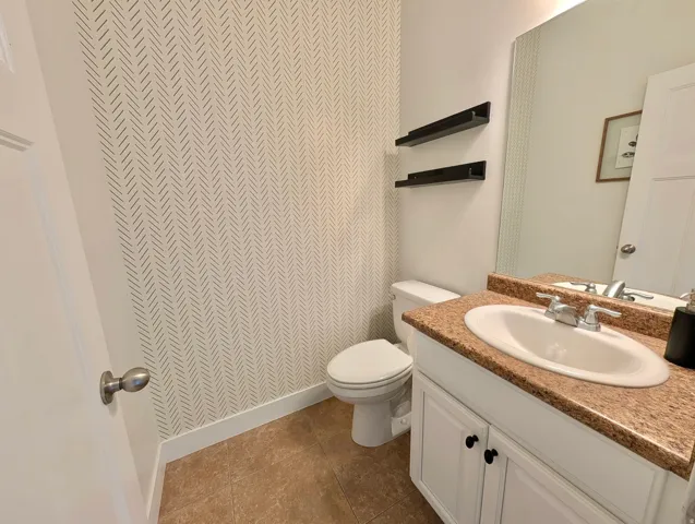 Powder room featuring a vanity with a white cabinet, integrated sink, and granite-style countertop
