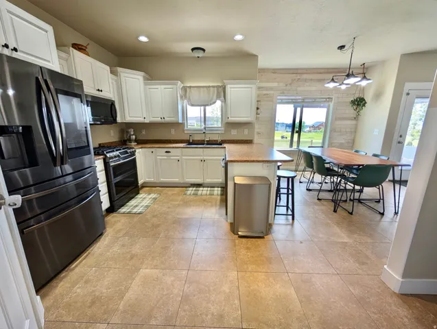 Open-concept kitchen and dining area featuring white cabinetry, a black appliance suite, and light-toned tile flooring