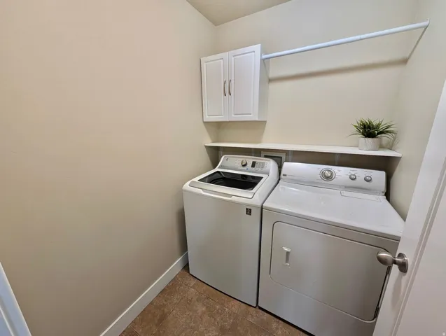 Dedicated laundry area featuring white upper cabinetry, a mounted clothes rod, a white wall shelf, and wood-finish flooring