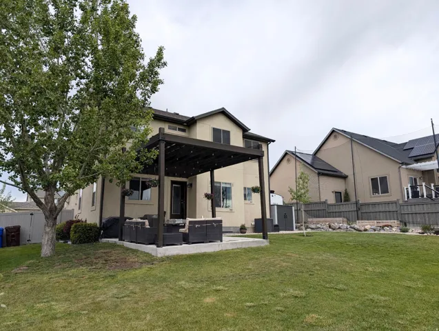 Spacious backyard featuring a substantial pergola-covered patio, mature trees, and raised garden beds