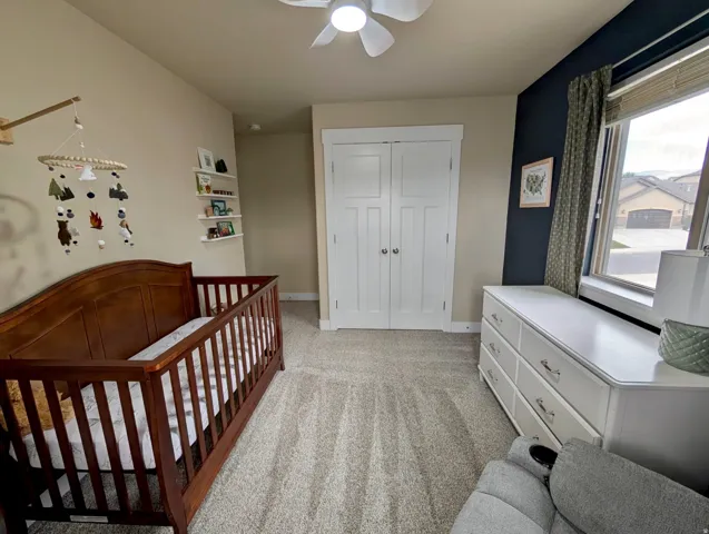 Carpeted room featuring a ceiling fan, a window with blinds, and a built-in closet with double doors