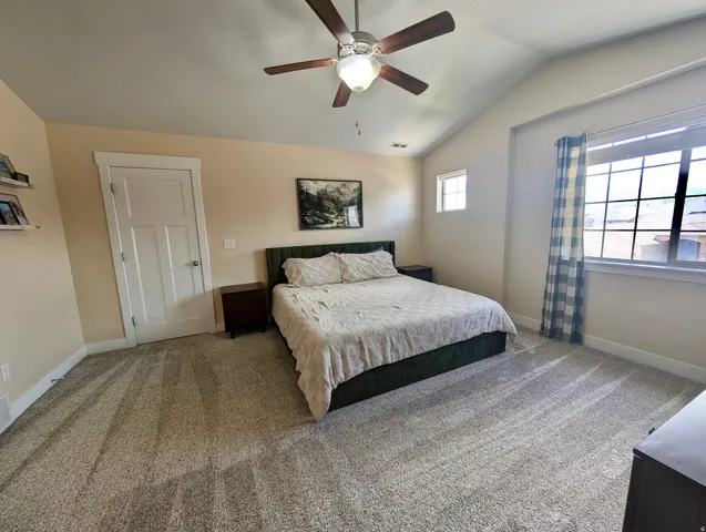 Spacious room featuring vaulted ceilings, a ceiling fan with integrated lighting, expansive windows, a three-panel interior door, and neutral-toned carpeting