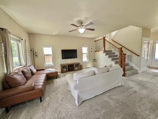 Bright living space featuring a carpeted floor, multiple windows providing natural illumination, and a ceiling fan