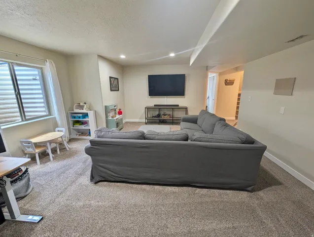 Carpeted living area featuring recessed lighting, a large window with blinds, and light-toned walls