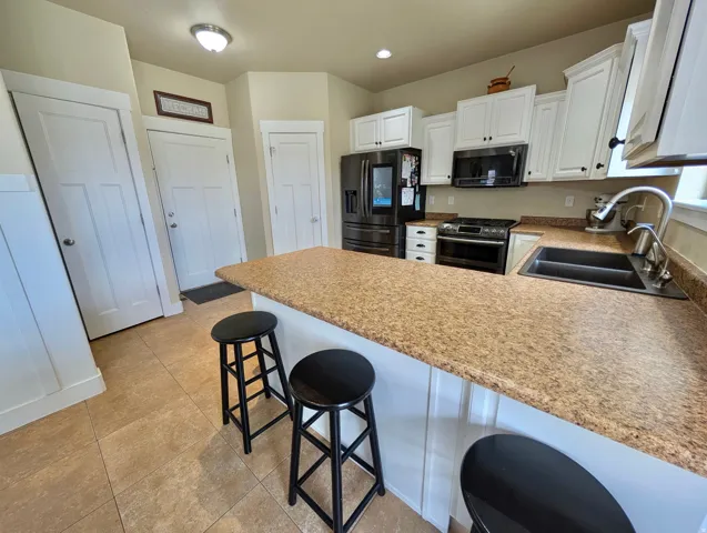Kitchen featuring a large breakfast bar with a speckled countertop, white cabinetry with black hardware, a dual-basin sink, and tile flooring