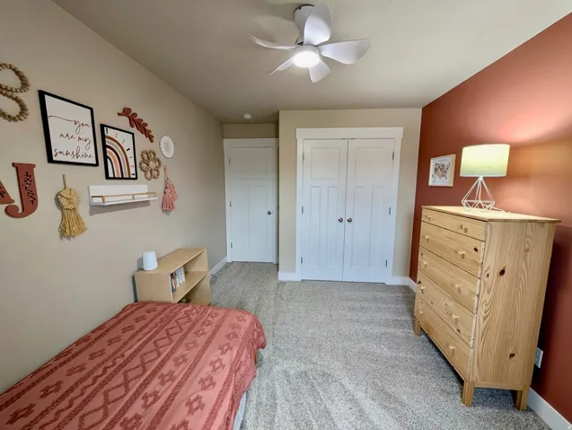 Bedroom featuring a built-in ceiling fan with light, plush carpet flooring, a two-door closet with white trim, a single paneled door, and a painted accent wall