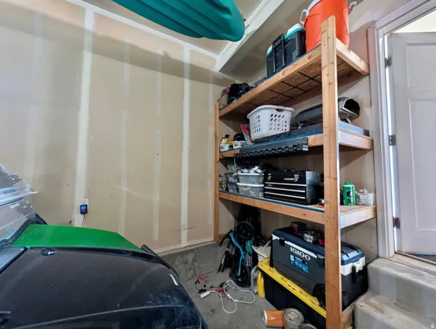 Utility shelving unit with four tiers, concrete flooring, and a white interior door with a threshold
