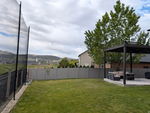 Expansive backyard featuring a manicured lawn, a large concrete patio with a built-in pergola, and a tall privacy fence